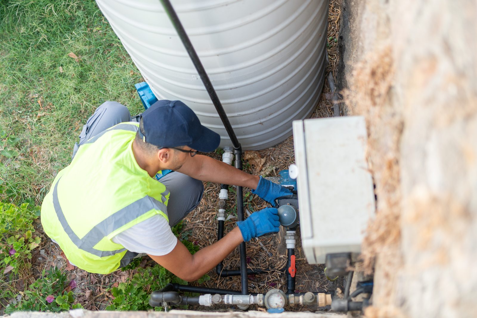 Technician repairing pipework and fittings at the base of a poly water tank